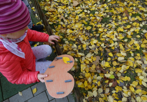 Dziewczynka zbiera liście, które dołączy do papierowego serduszka za pomocą drewnianej klamerki.